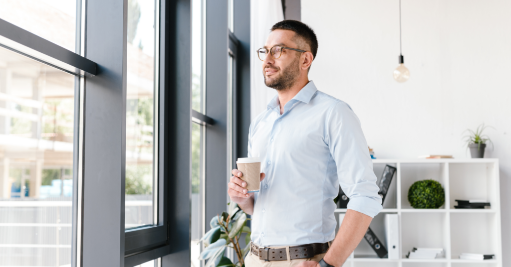 Business man looking outside window with coffee in hand.