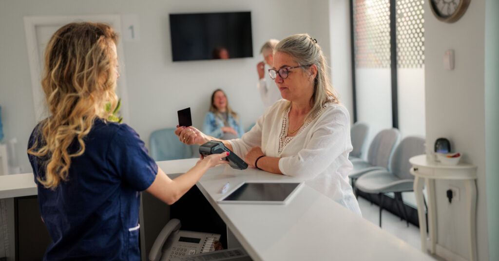 Woman paying the receptionist at a medical office via credit card.