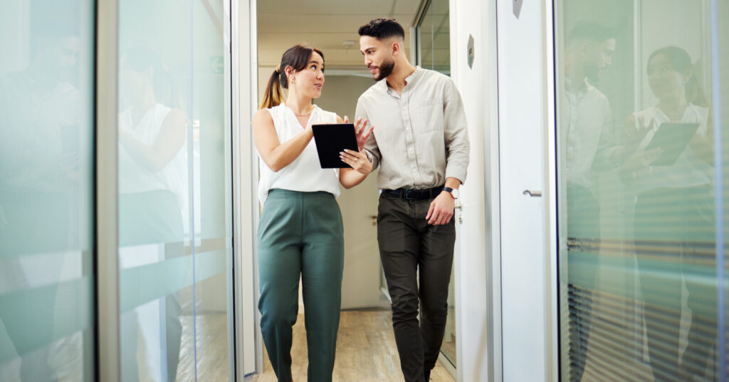 A man and woman walk down an office hallway