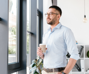 Business man looking outside window with coffee in hand.
